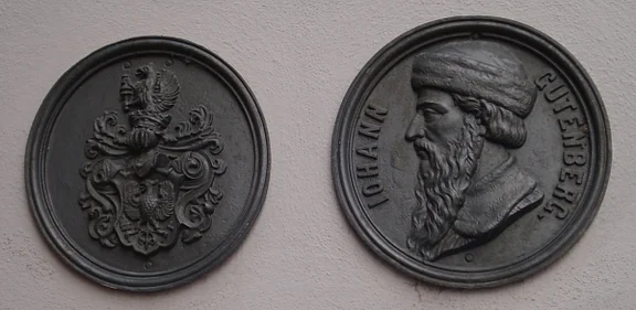 Plaketten mit Wappen und Johann Gutenberg, den Erfinder der Buchdruckkunst, an der Südseite des Hauses, Oktober 2009. Diese Plaketten befanden sich früher an der Ostseite (Straßenseite) über den Erdgeschoss-Fenstern. Foto: Daniel Stihler (StadtA Server Häuserlexikon)