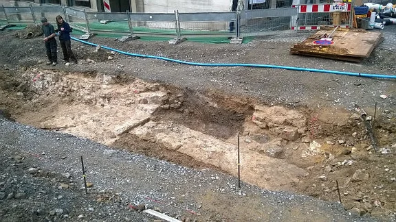 Bei Bauarbeiten entdeckte Fundamente des Stätt-Tors (links), der Stadtmauer und der davor (rechts) verlaufenden Zwingermauer nach Freilegung durch Mitarbeiter des Landesdenkmalamts Baden-Württemberg. Längs des Grabens verlaufen die Fundamente der östlichen Seitenmauer eines dem eigentlichen Torturm vorgelagerten Vortors. Blick aus Richtung Osten vom Wachhaus aus. 12.4.2016. Foto: Daniel Stihler (StadtA Schwäb. Hall DIG 7533)