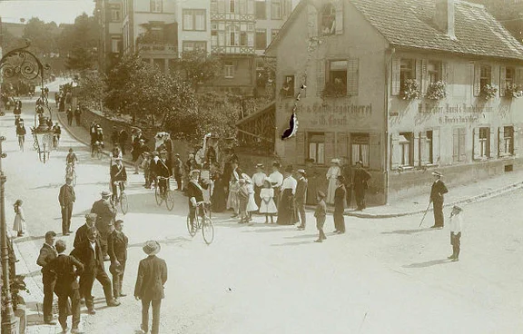 Festumzug eines Fahrradvereins, vermutlich des 1898 gegründeten „Radfahrer-Clubs“, rechts im Hintergrund das Haus Bahnhofstraße 26. Undatiertes Foto um 1900, Fotograf unbekannt (StadtA Schwäb. Hall FS 54368)
